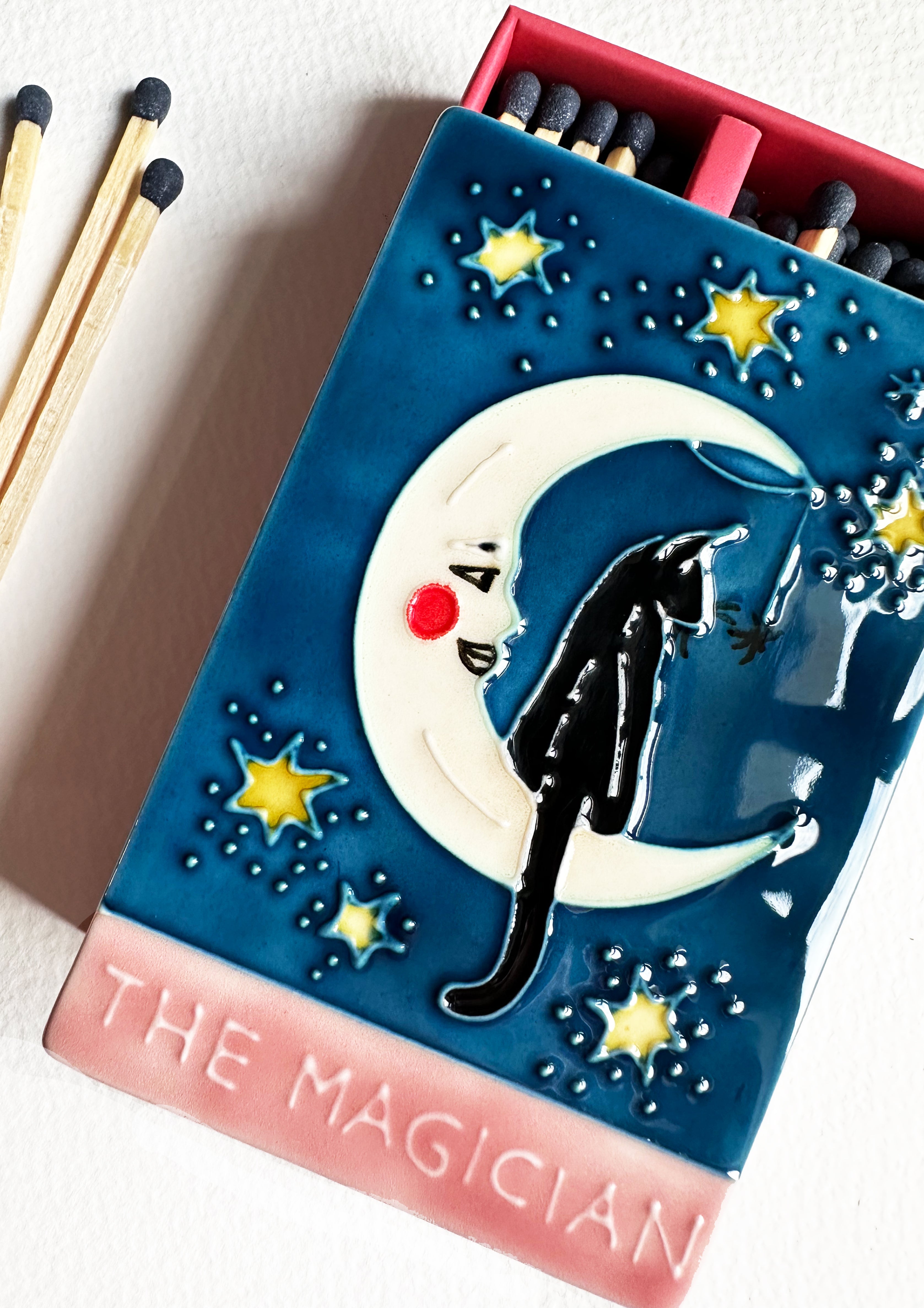 Luxury ceramic matchbox featuring The Magician Tarot card - a black cat sits within a crescent moon. The ceramic artwork sits atop a luxury card case with striker strip. Each box contains 40 navy coloured extra long safety matches.