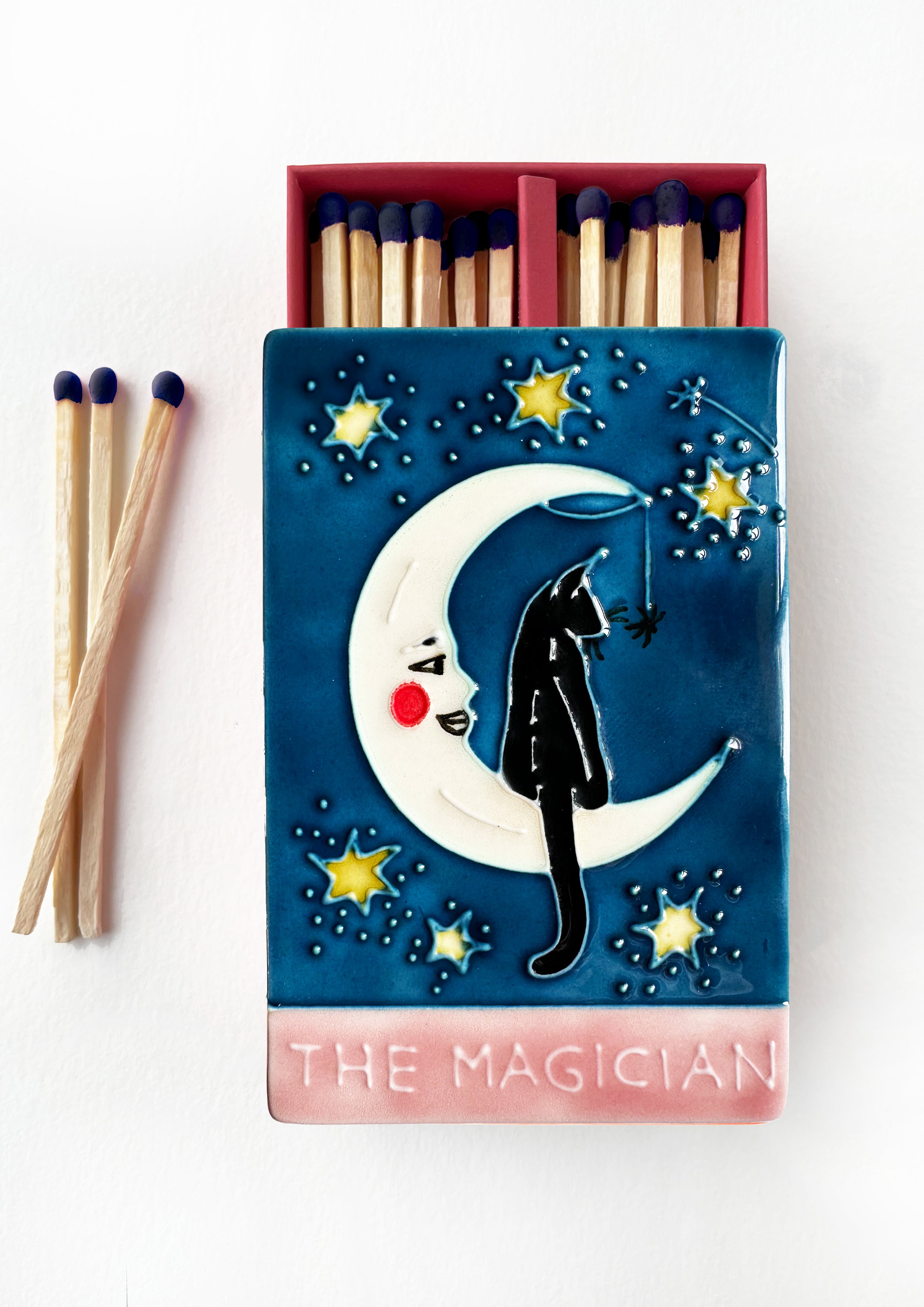 Luxury ceramic matchbox featuring The Magician Tarot card - a black cat sits within a crescent moon. The ceramic artwork sits atop a luxury card case with striker strip. Each box contains 40 navy coloured extra long safety matches.