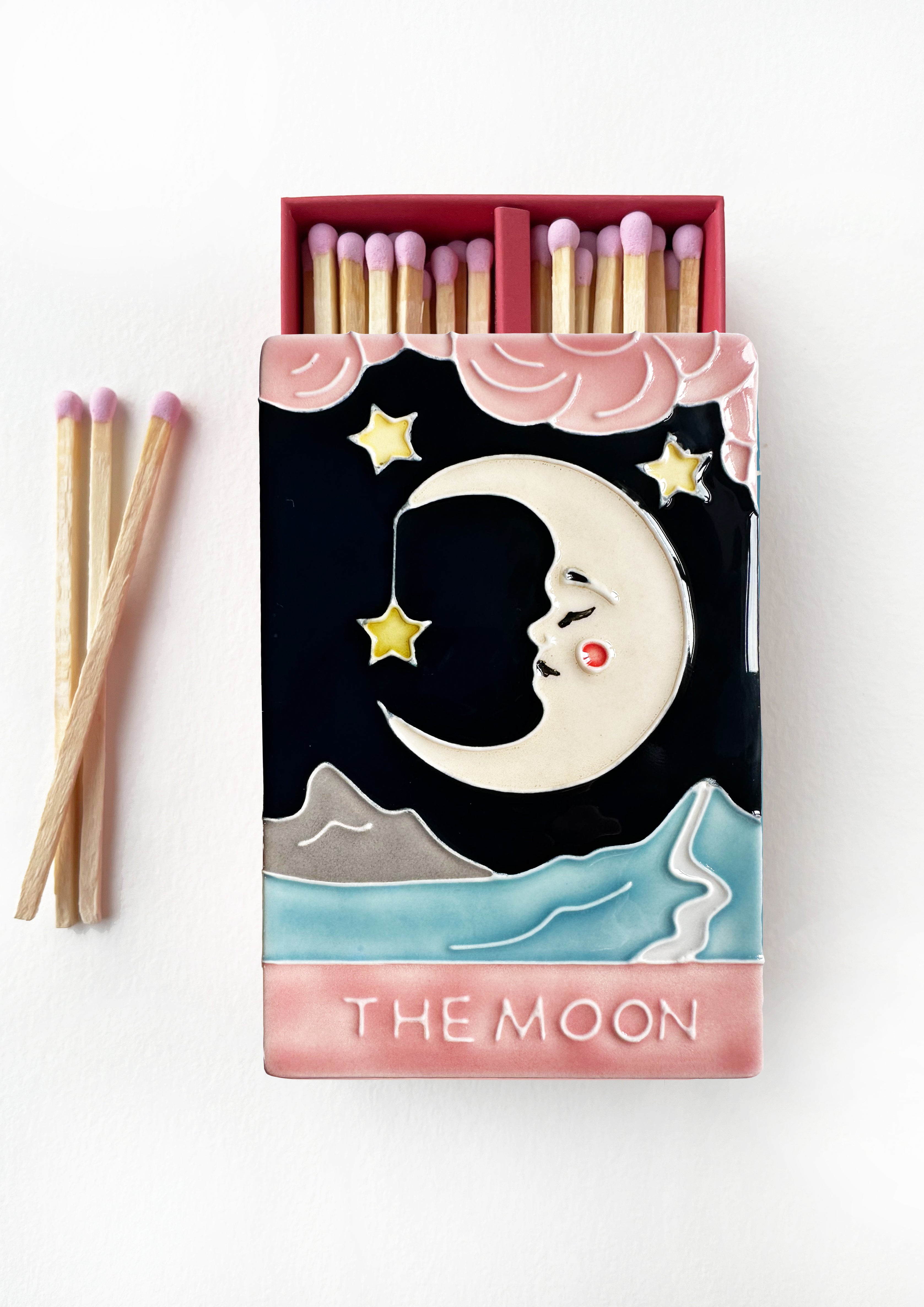 Bestselling luxury ceramic matchbox featuring The Moon Tarot card. The ceramic artwork sits atop a luxury card case with striker strip. Each box contains 40 navy coloured extra long safety matches. Made exclusively in England.