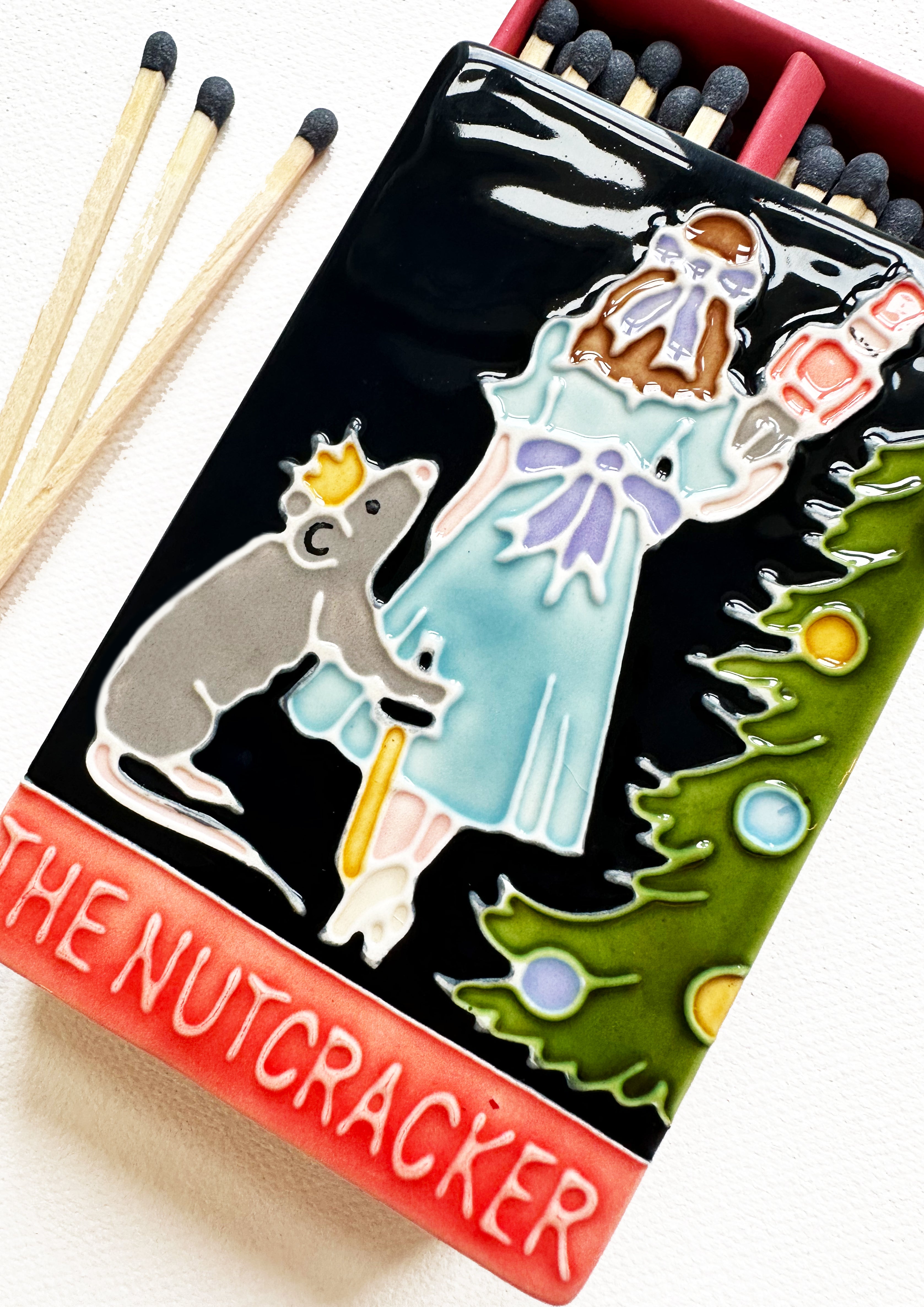 Luxury ceramic matchbox featuring the iconic Nutcracker ballet scene. The ceramic artwork sits atop a luxury card case with striker strip. Each box contains navy coloured extra long safety matches. Made exclusively in England.