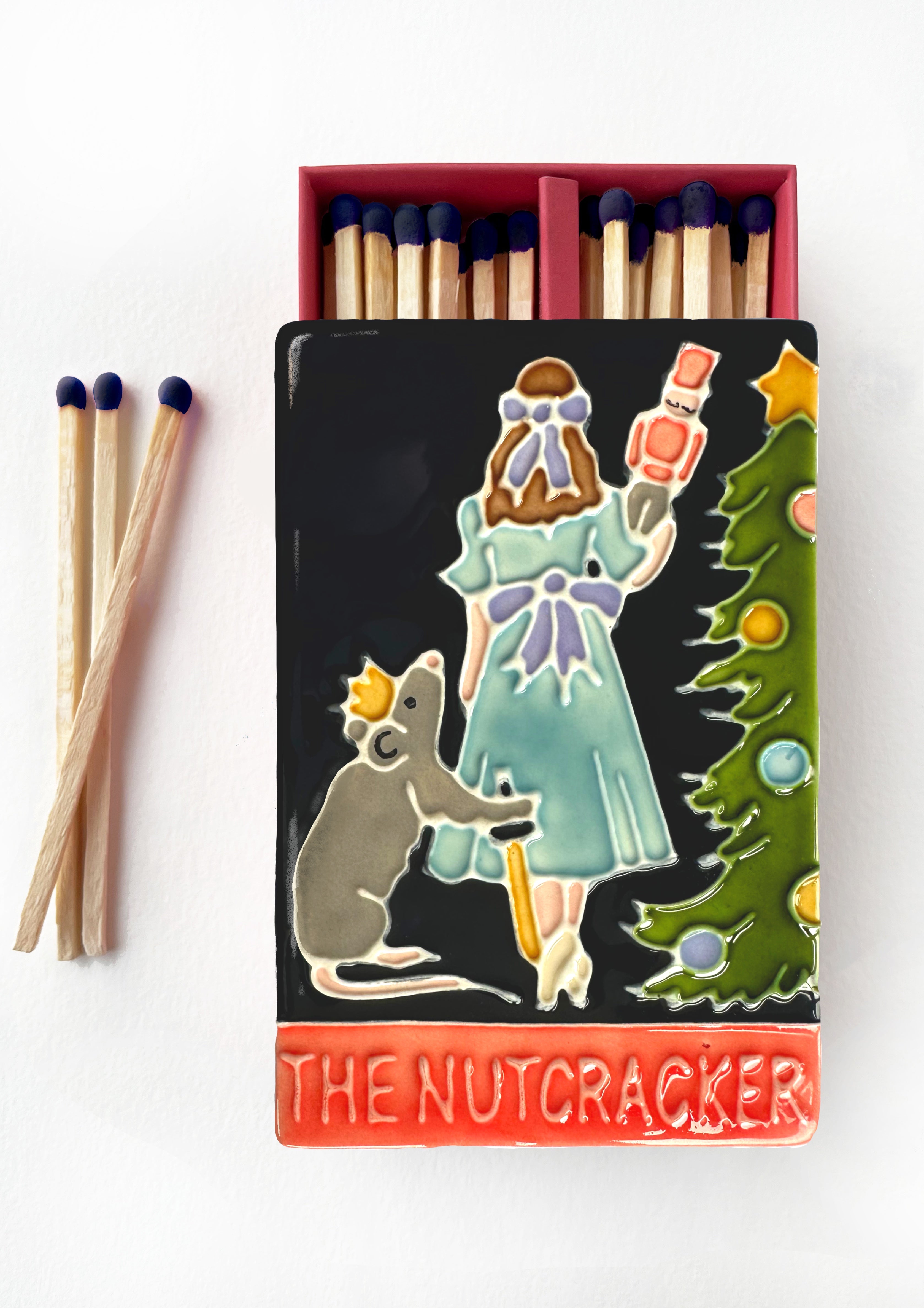 Luxury ceramic matchbox featuring the iconic Nutcracker ballet scene. The ceramic artwork sits atop a luxury card case with striker strip. Each box contains navy coloured extra long safety matches. Made exclusively in England.