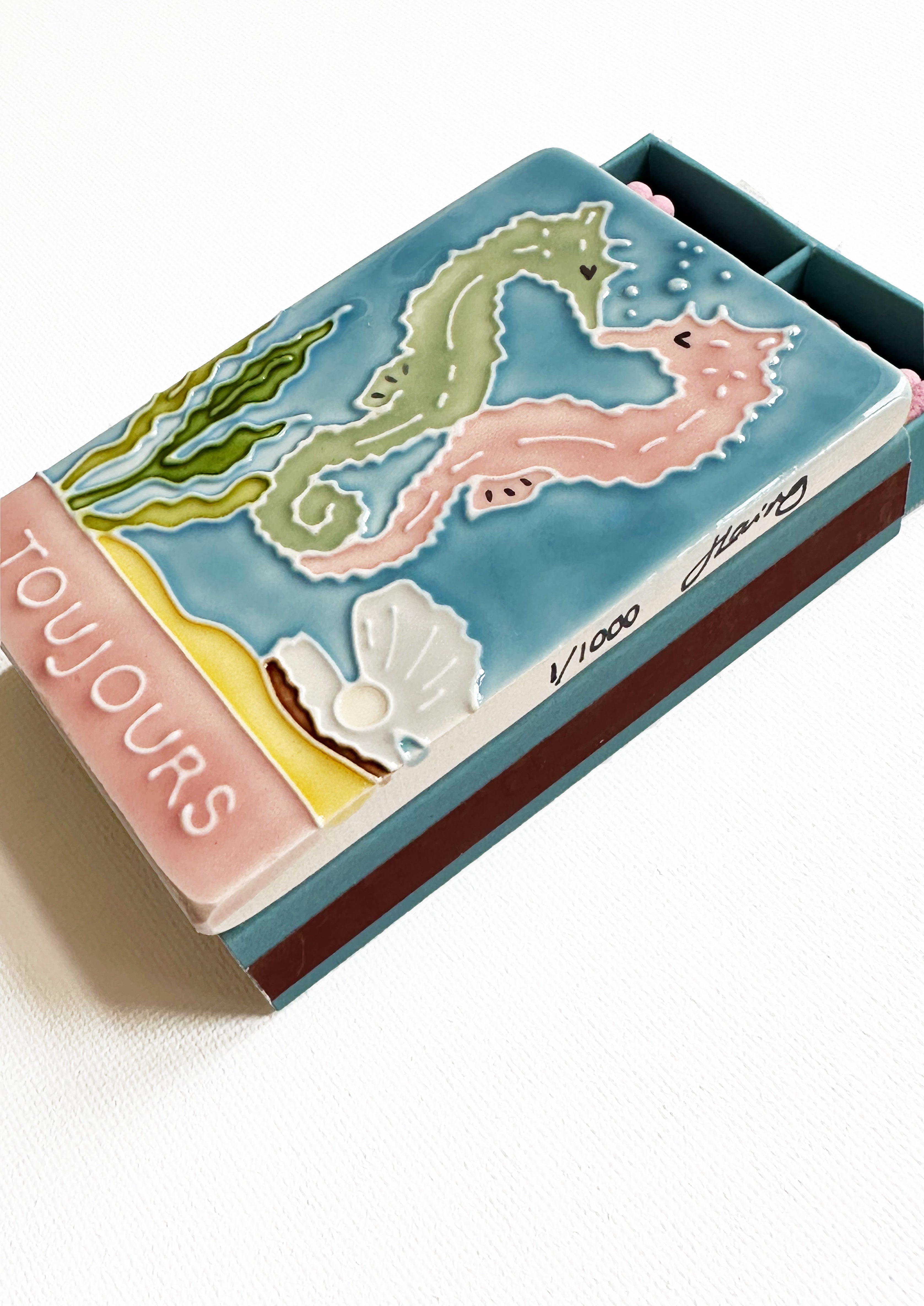 Luxury ceramic matchbox featuring kissing seahorses. The ceramic artwork sits atop a luxury card case with striker strip. Each box contains 40 peach coloured extra long safety matches.