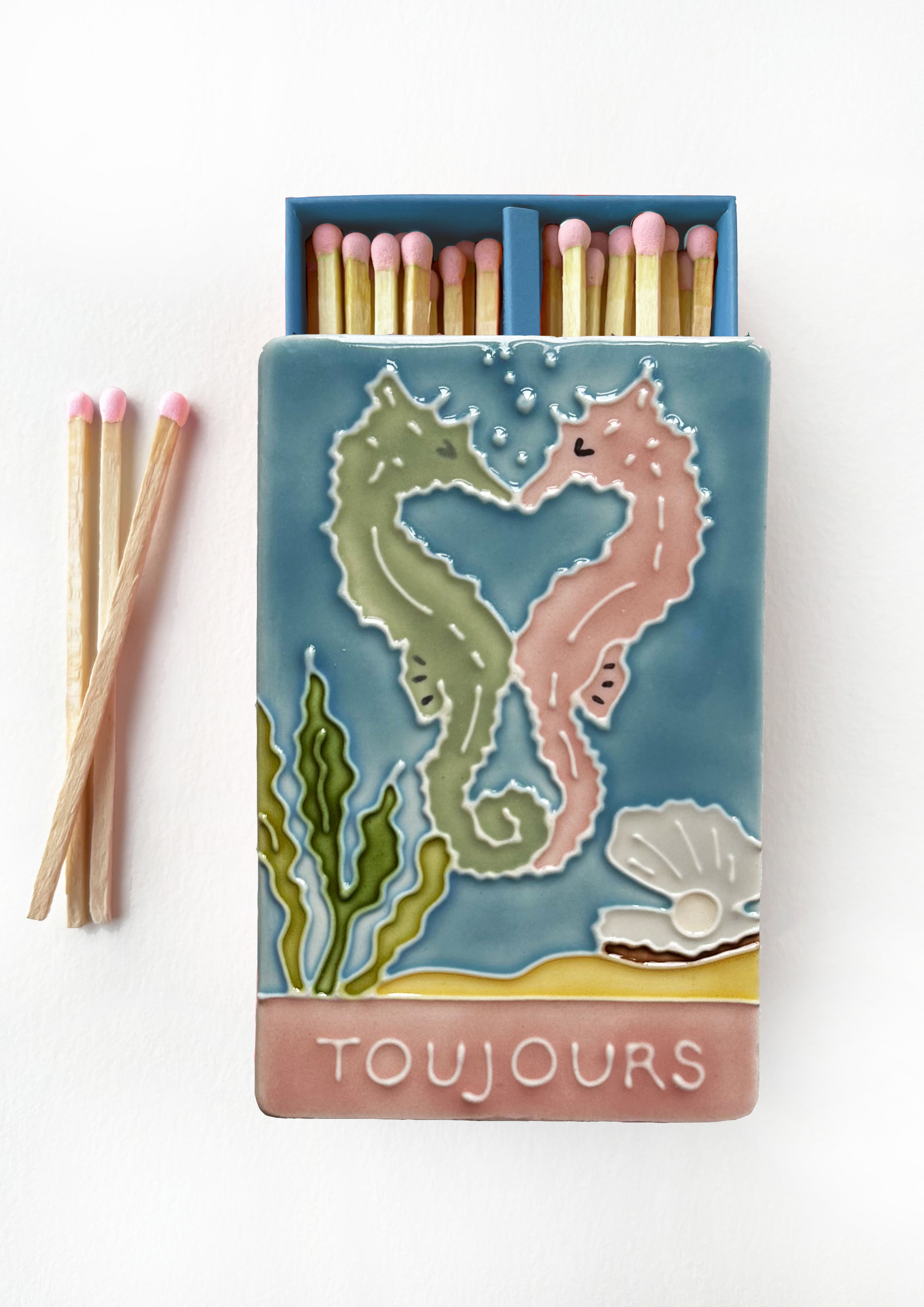 Luxury ceramic matchbox featuring kissing seahorses. The ceramic artwork sits atop a luxury card case with striker strip. Each box contains 40 peach coloured extra long safety matches.