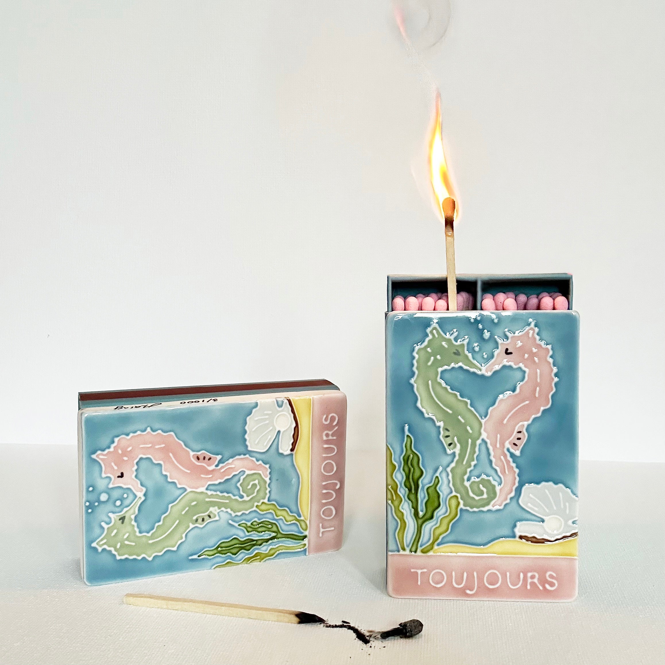 Luxury ceramic matchbox featuring kissing seahorses. The ceramic artwork sits atop a luxury card case with striker strip. Each box contains 40 peach coloured extra long safety matches.