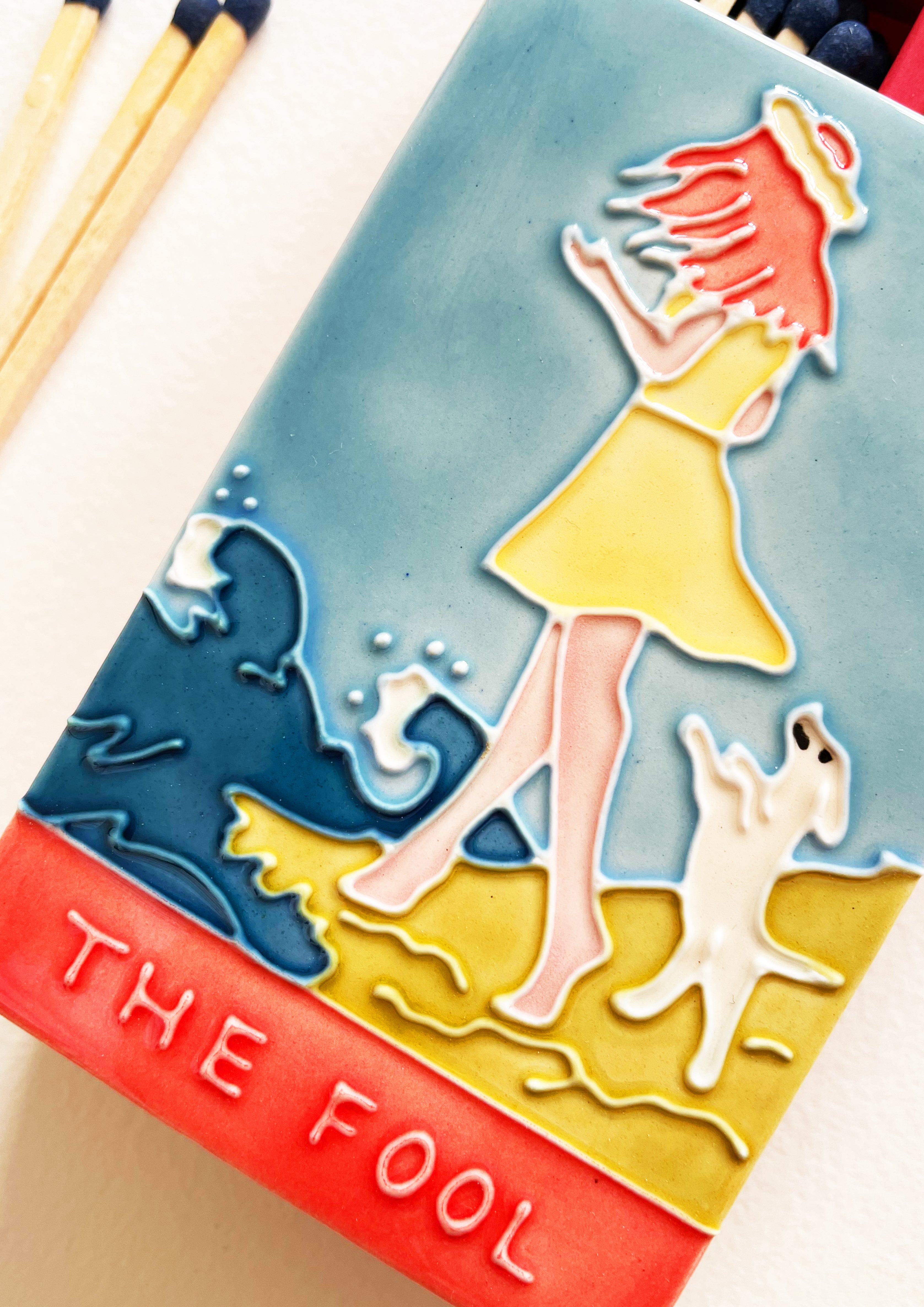 Luxury ceramic 'Moi et Toi' matchbox featuring the Fool tarot card. The ceramic artwork sits atop a luxury card case with striker strip. Each box contains 40 navy coloured extra long safety matches. Made exclusively in England.