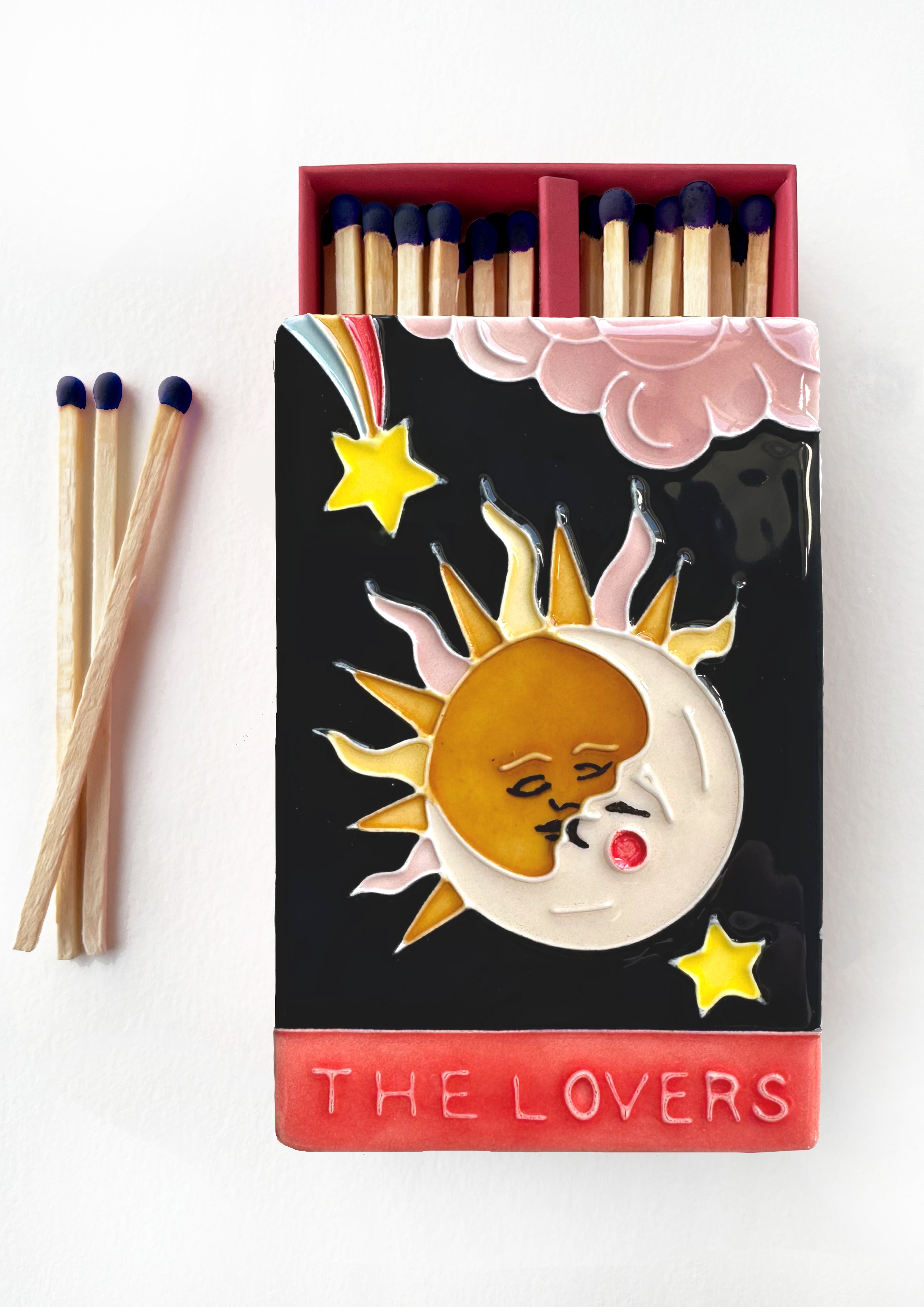 Bestselling luxury ceramic matchbox featuring The Lovers Tarot card - a sun and moon kiss in the night sky. The ceramic artwork sits atop a luxury card case with striker strip. Each box contains 40 navy coloured extra long safety matches. Made exclusively in England.