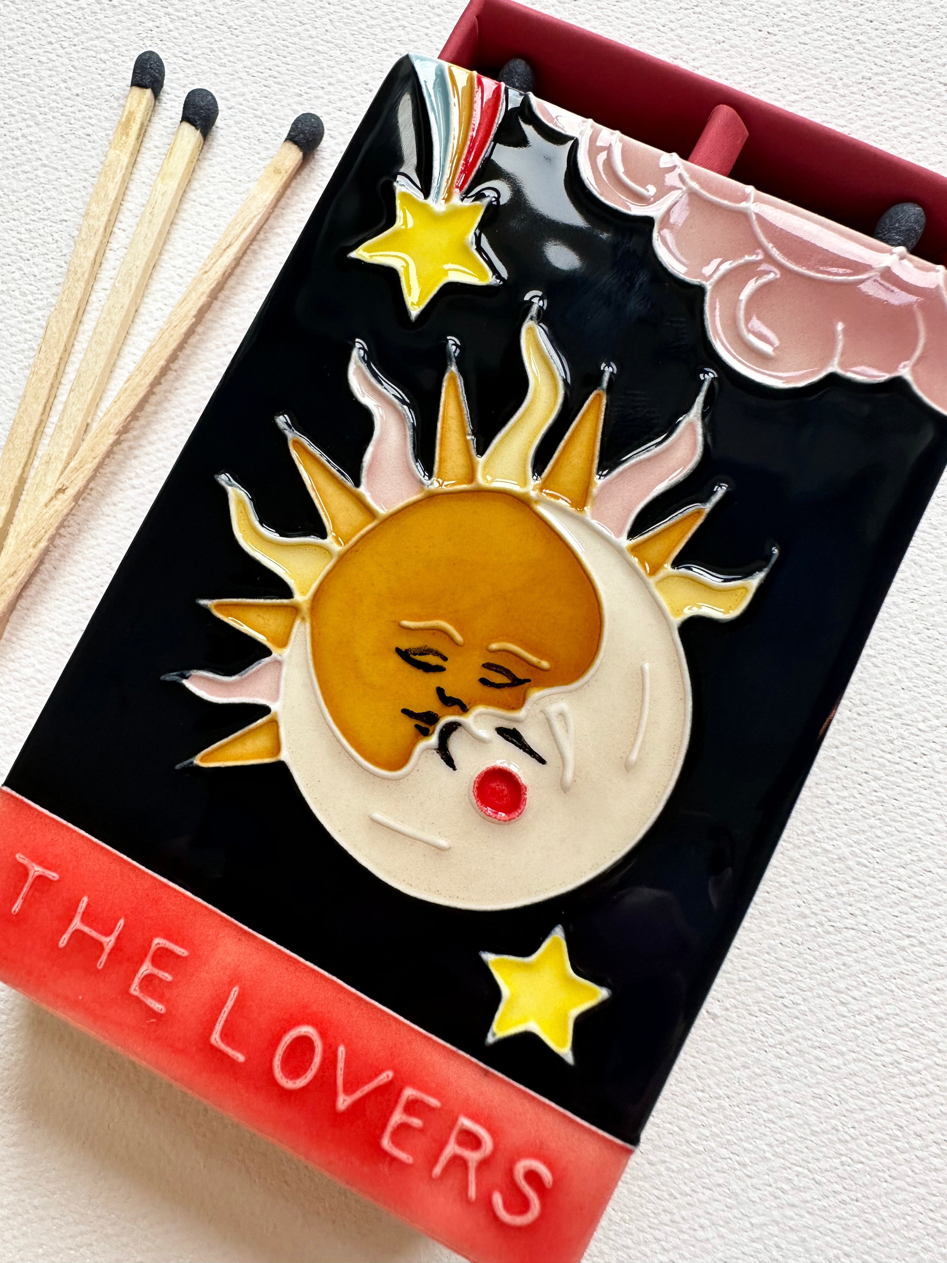 Bestselling luxury ceramic matchbox featuring The Lovers Tarot card - a sun and moon kiss in the night sky. The ceramic artwork sits atop a luxury card case with striker strip. Each box contains 40 navy coloured extra long safety matches. Made exclusively in England.