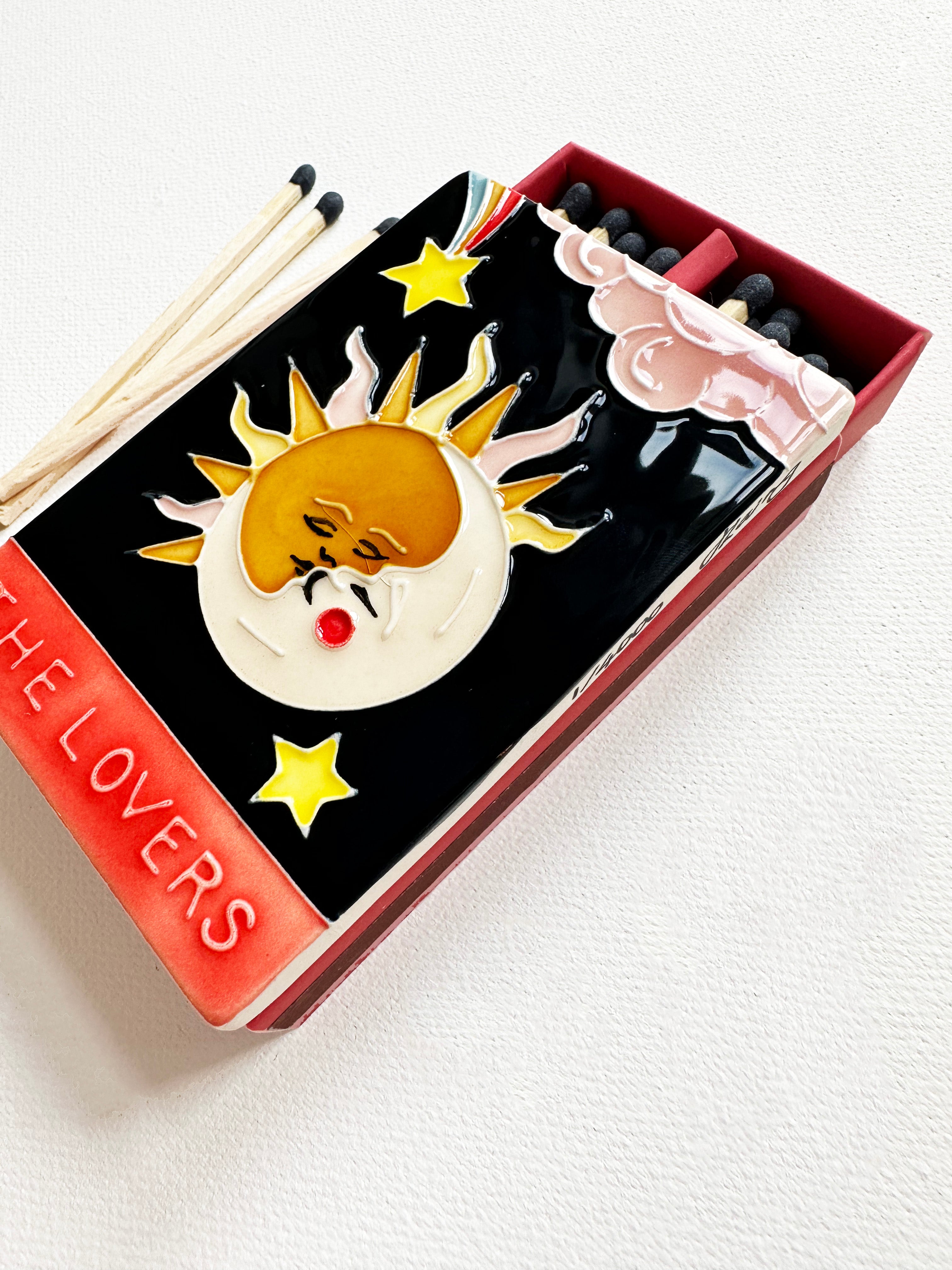 Bestselling luxury ceramic matchbox featuring The Lovers Tarot card - a sun and moon kiss in the night sky. The ceramic artwork sits atop a luxury card case with striker strip. Each box contains 40 navy coloured extra long safety matches. Made exclusively in England.