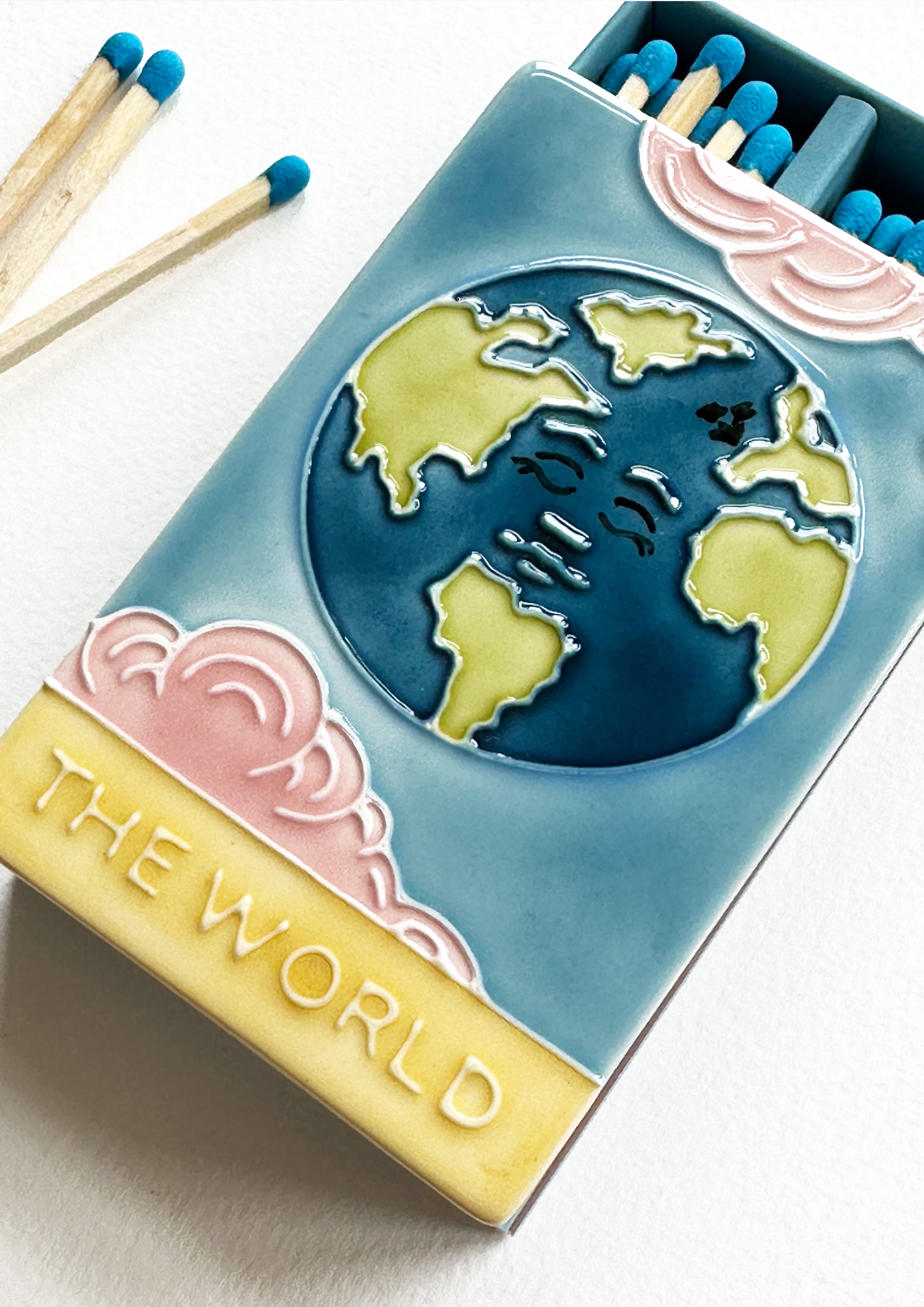 Bestselling luxury ceramic matchbox featuring The World Tarot card. The ceramic artwork sits atop a luxury card case with striker strip. Each box contains 40 aqua coloured extra long safety matches. Made exclusively in England.