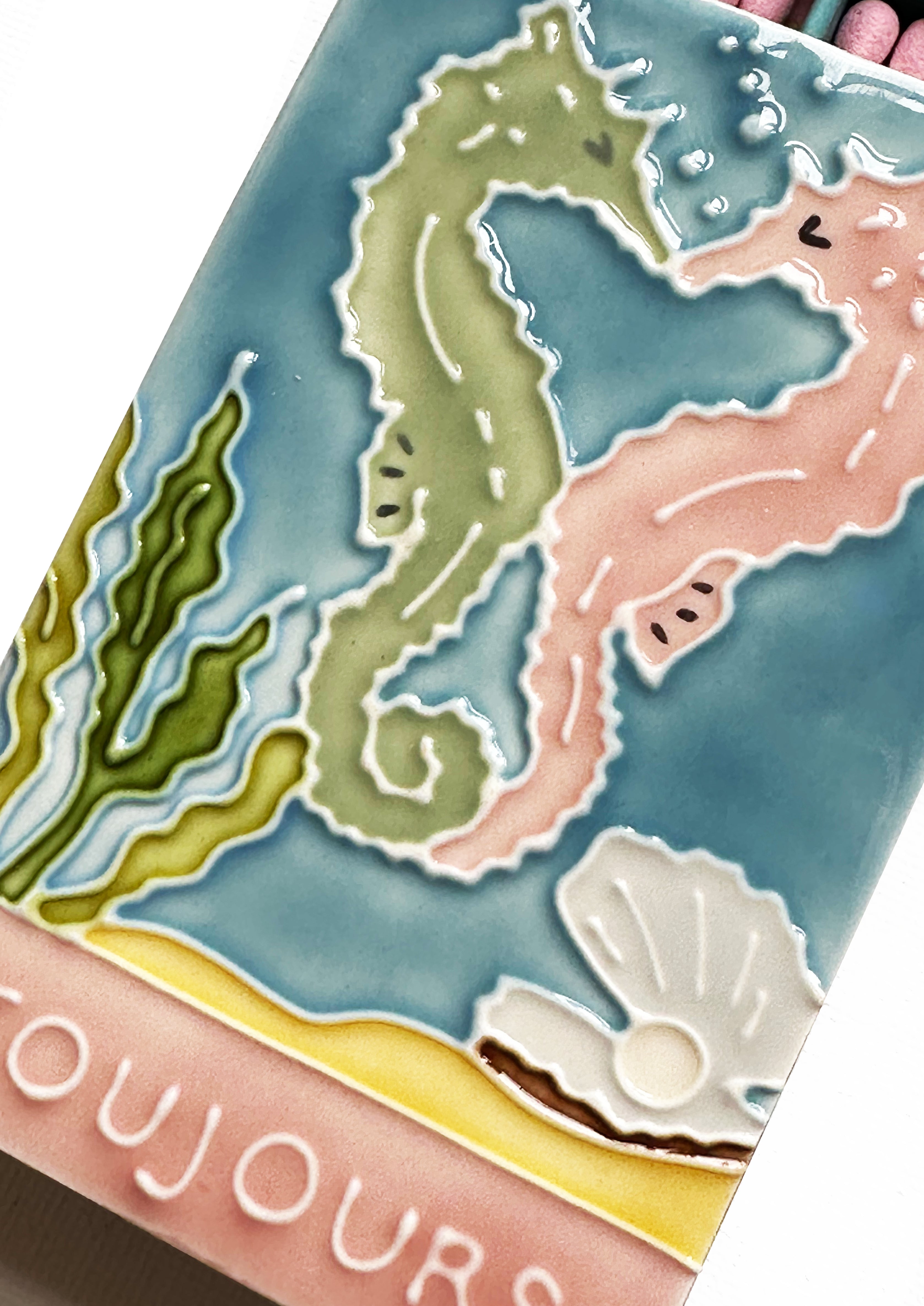 Luxury ceramic matchbox featuring kissing seahorses. The ceramic artwork sits atop a luxury card case with striker strip. Each box contains 40 peach coloured extra long safety matches.