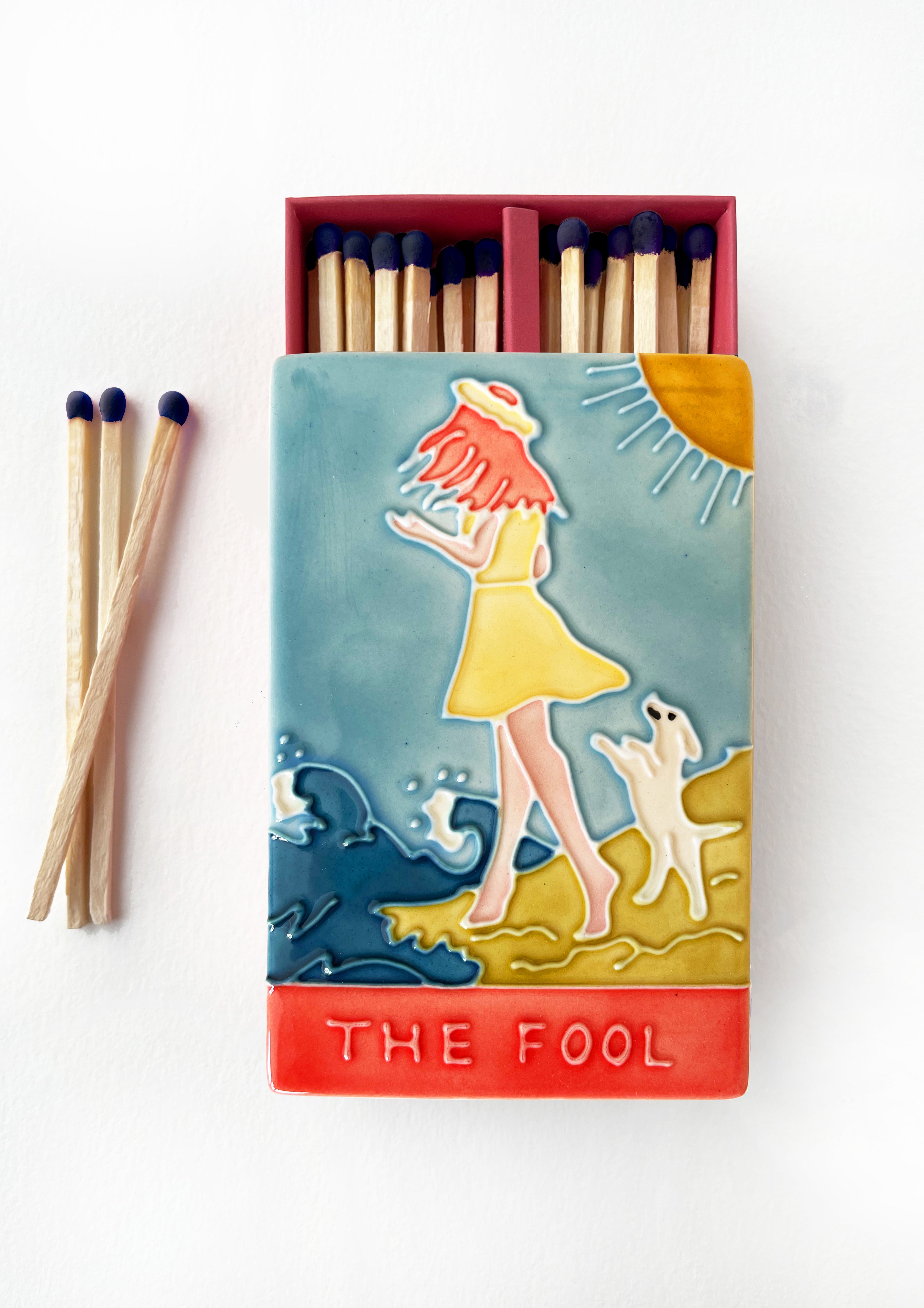 Luxury ceramic 'Moi et Toi' matchbox featuring the Fool tarot card. The ceramic artwork sits atop a luxury card case with striker strip. Each box contains 40 navy coloured extra long safety matches. Made exclusively in England.